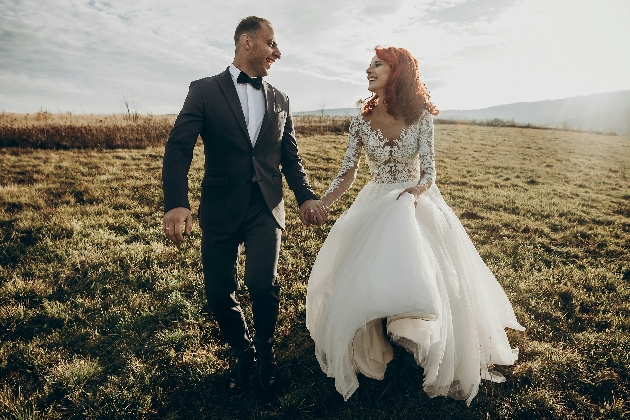 A bride and groom walking hand-in-hand in a field